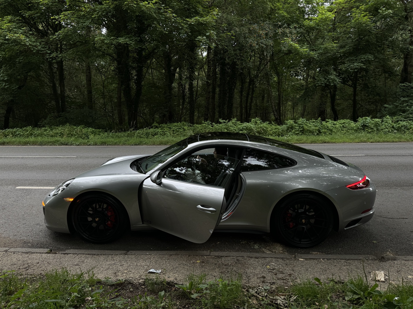 Η 911 GTS σταματημένη στην άκρη του δρόμου με την πόρτα ανοιχτή, μπροστά από δάσος