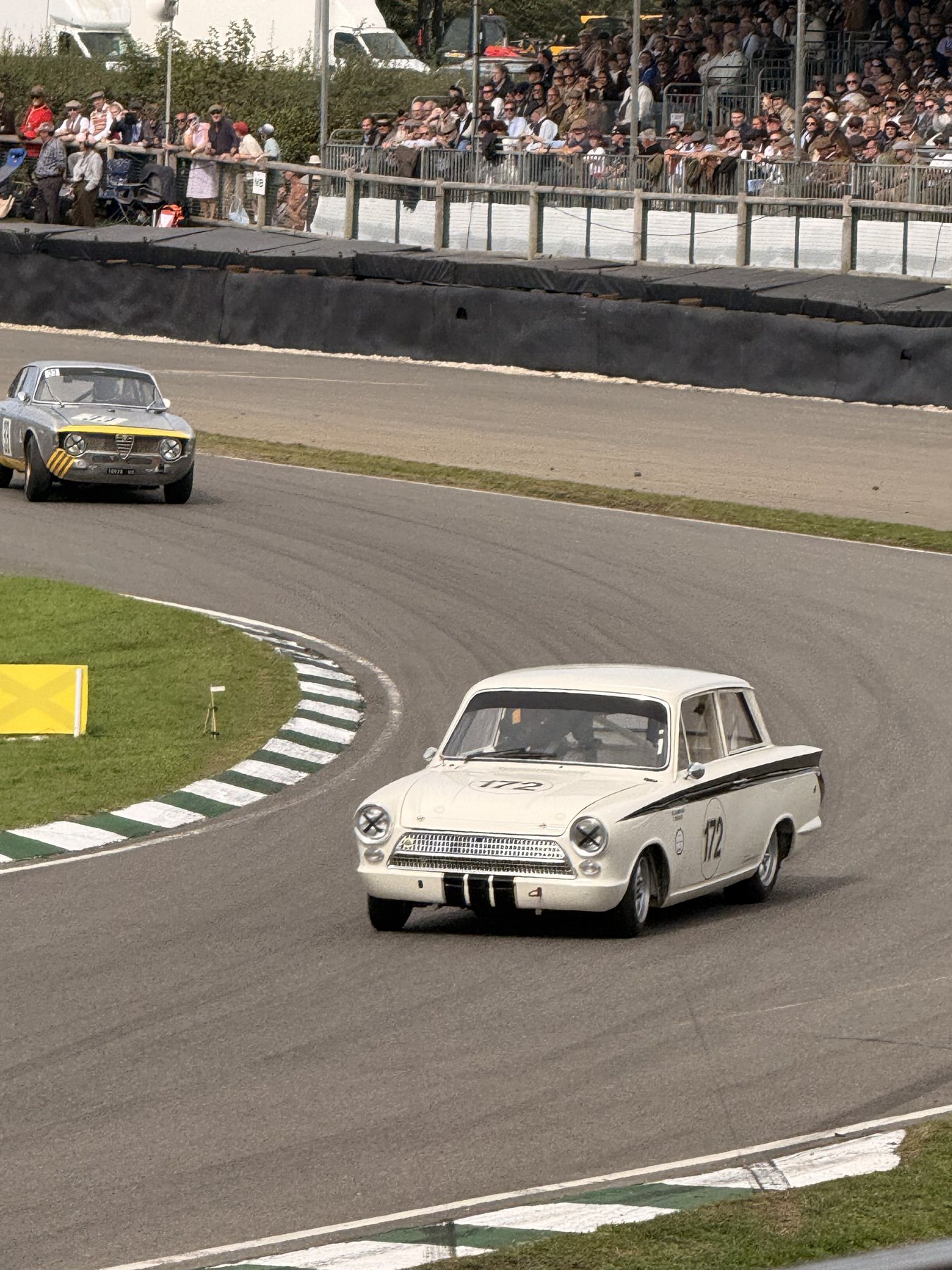 Λευκή Lotus Cortina με μαύρη ρίγα και νούμερο 172 στη στροφή, με κόσμο στην εξέδρα πίσω