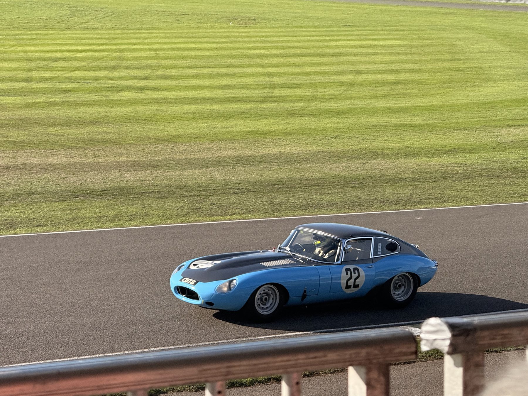 Γαλάζια Jaguar E-type coupé με νούμερο 22 στη στροφή, με γρασίδι πίσω της