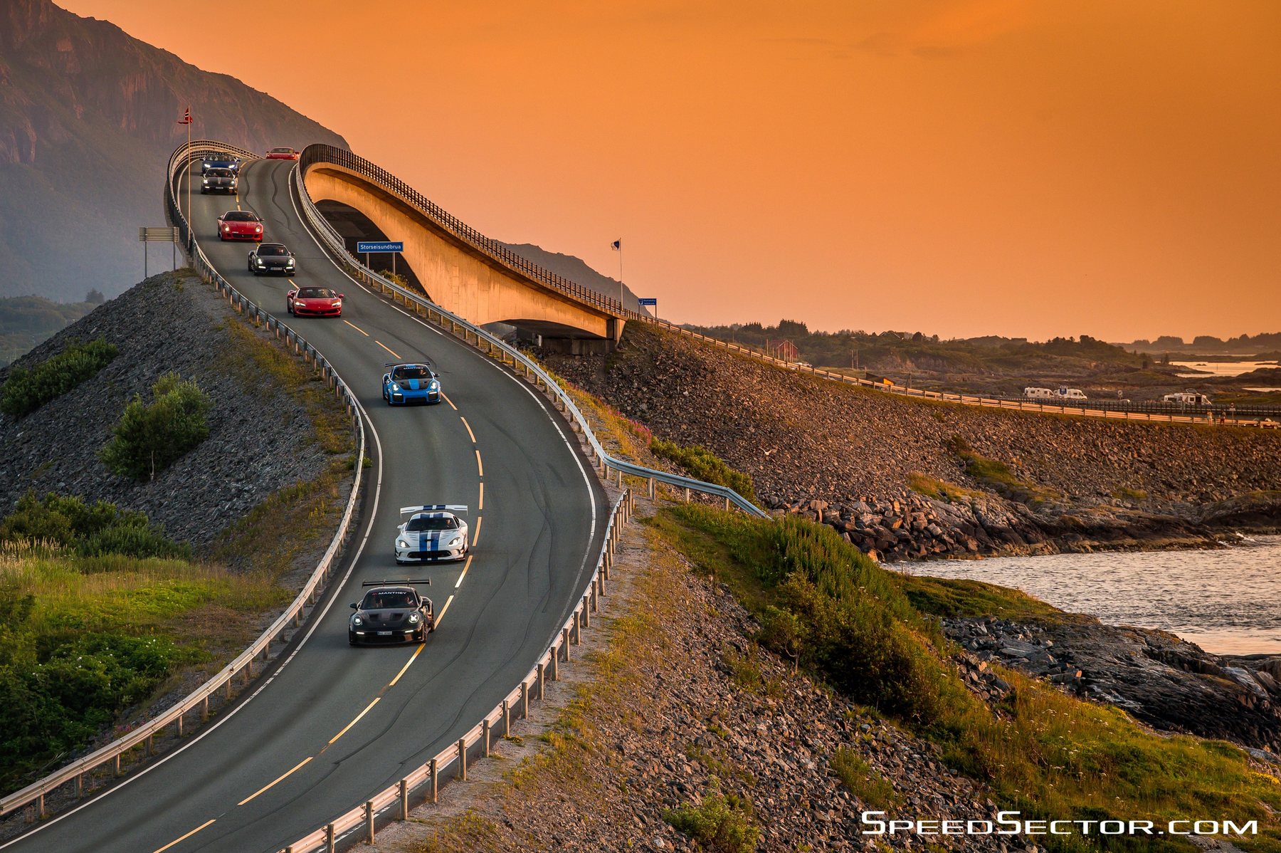 Η γέφυρα του Atlantic Road ανεβαίνει πάνω από τη θάλασσα το ηλιοβασίλεμα, με μια σειρά αυτοκίνητα να την περνούν