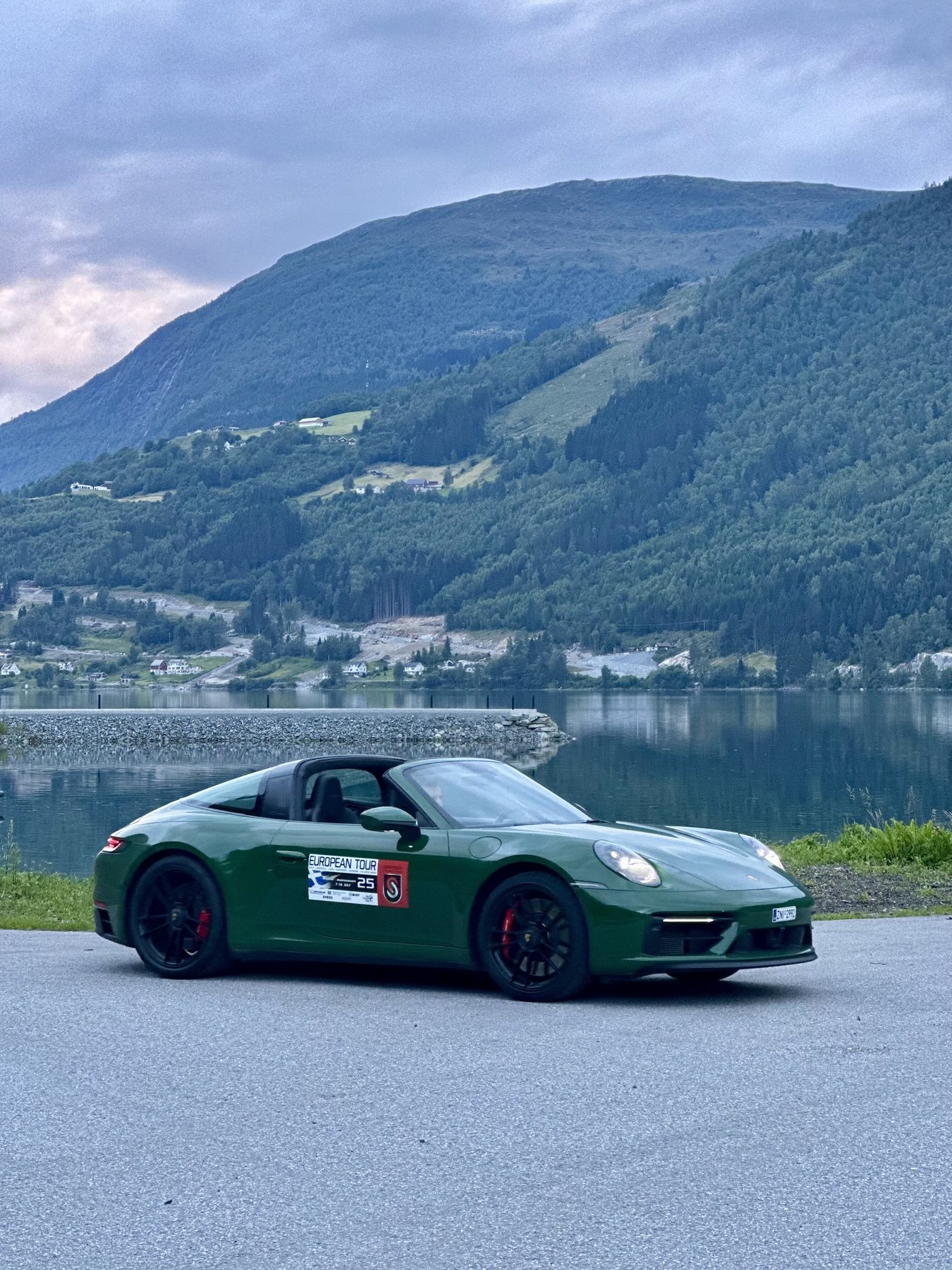 Η πράσινη 911 Targa παρκαρισμένη στην άκρη δρόμου δίπλα σε fjord, με βουνό απέναντι