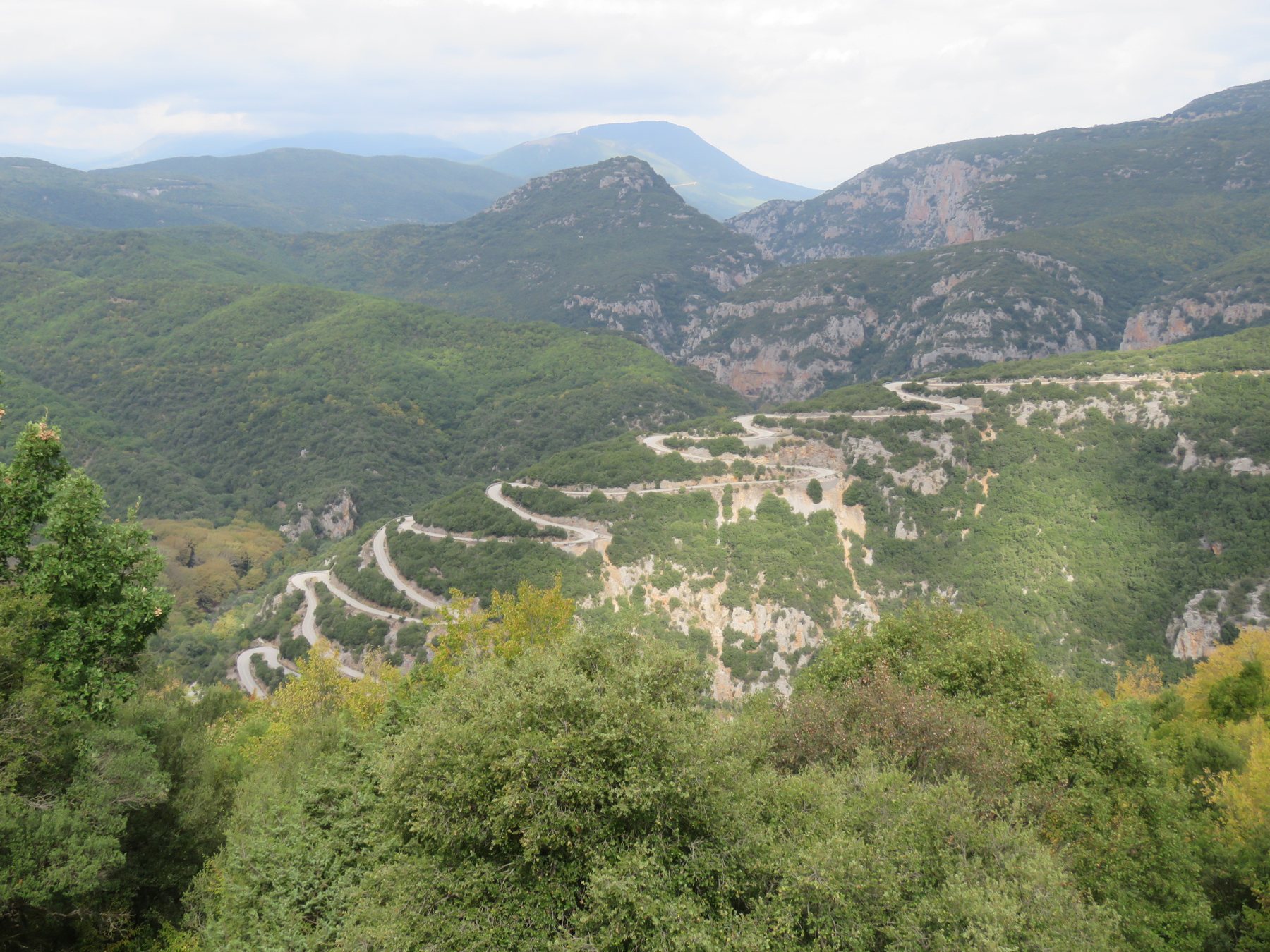The successive hairpins of the Aristi to Papingo road on the wooded slope, mountains in the background