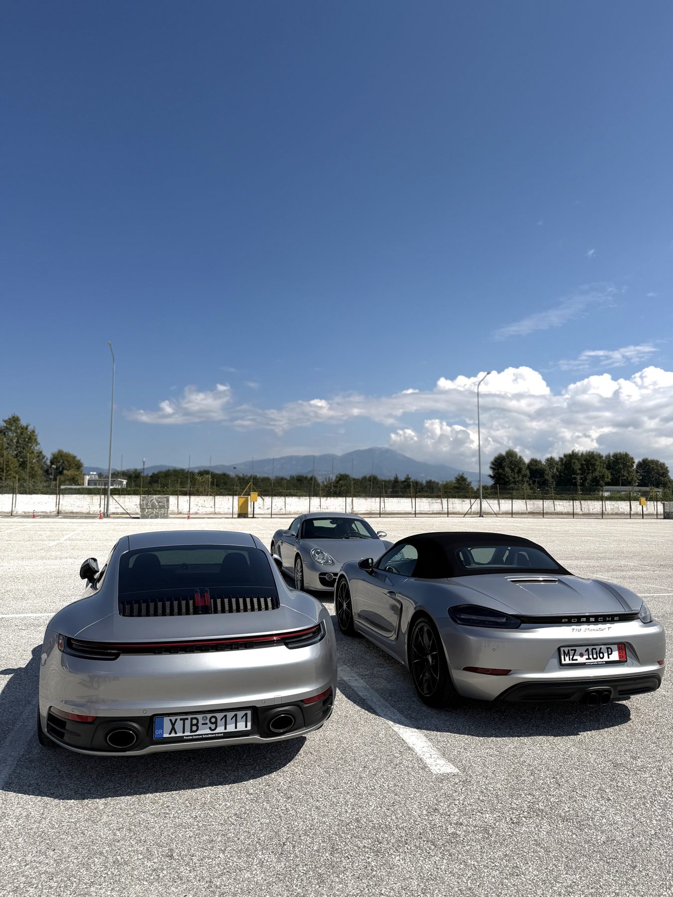 Τρεις GT Silver Porsche παρκαρισμένες σε σειρά: 992 Carrera, 718 Boxster T και Cayman S 987.1