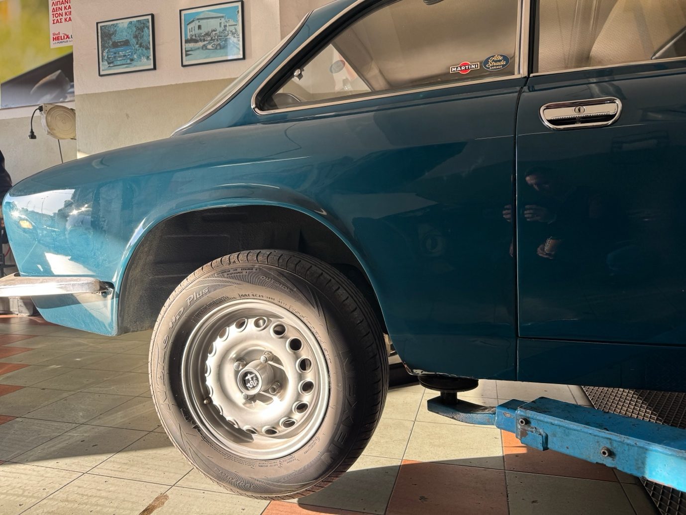 Η μπλε Alfa Romeo GT 1300 Junior Bertone σε προφίλ, ανεβασμένη στο αναβατόριο του συνεργείου